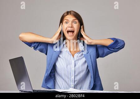 an angry businesswoman at workplace, talking on two smartphones at once Stock Photo
