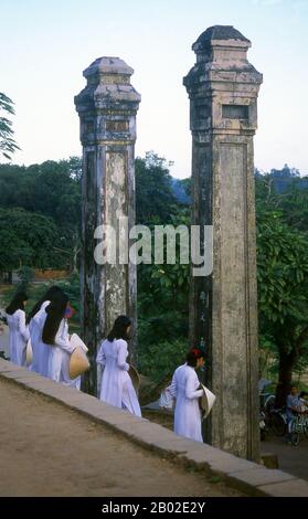 Vietnam: Students in traditional Vietnamese ao dai ('long dress') and non la (conical hat) at the Thien Mu (Thiên Mụ) Pagoda, Hue. Thien Mu Pagoda was built in 1601 CE under Nguyen Hoang, the governor of Thuan Hoa province, now known as Hue. Although he swore loyalty to the Le Dynasty in Hanoi, Nguyen Hoang effectively ruled Thuan Hoa as an independent state in central Vietnam. The pagoda has seven storeys and is the tallest in Vietnam, and is often the subject of folk rhymes and poetry about Hue, which was the imperial capital of Vietnam between 1802 and 1945. Stock Photo