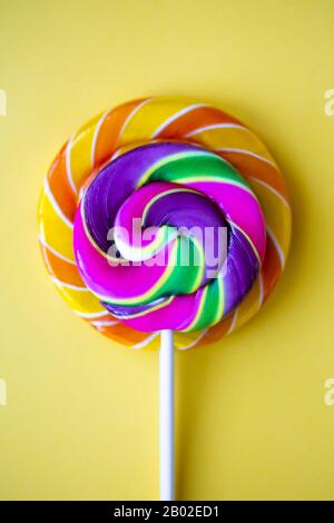 Bright swirl lollipops on yellow background. Festive vertical background with colorful twisted candies. Close up of rainbow round sweets on stick. Ora Stock Photo