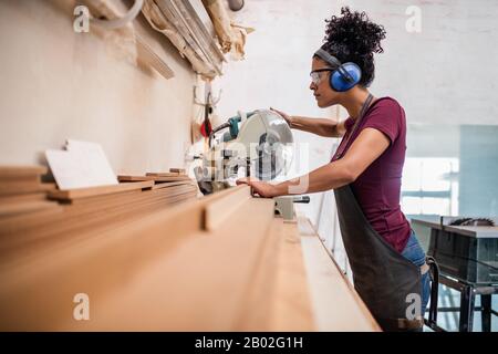 Female artisan sawing wood for frames in her workshop Stock Photo
