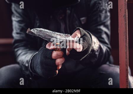 Drug addict smoking opium on tin foil, aka chasing the dragon, close up of hands with selective focus Stock Photo