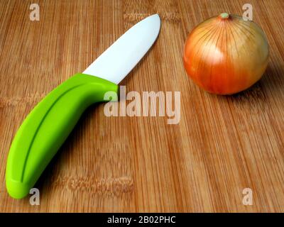 natural bamboo kitchen cutting board. white porcelain chopping and cutting knife. green ergonomic plastic handle & fresh brown golden green onion. Stock Photo