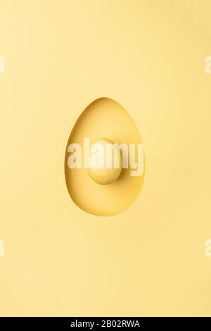 Pastel yellow color background with egg shaped hole. Monochrome Happy Easter minimal greeting card concept. Flat lay, top view, copy space Stock Photo