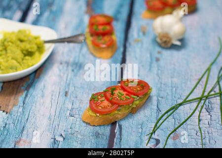 Open sandwich and a few chives scapes... two sandwiches, a bowl with avocado spread, and a garlic bulb are visible in a blurry background. Stock Photo