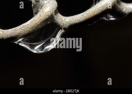 Abstract macro of a drop of water hanging from an iron chain Stock Photo
