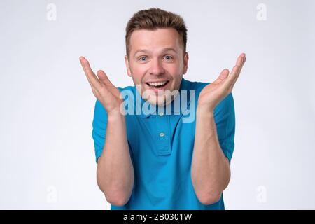 Excited casual man standing with raised hands and looking at camera with surprise. Studio shot. Positive facial human emotion. Stock Photo