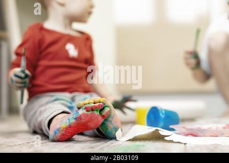 Adorable cute caucasian little blond siblings children enjoy having fun painting with brush and palm at home indoors . Cheerful happy kids smiling Stock Photo