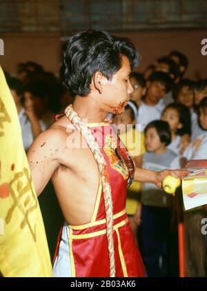 Thailand: A possessed spirit medium or ma song, The Nine Emperor Gods Festival, Chao Mae Thapthim Shrine (Taoist Chinese joss house), Wang Burapha, Bangkok (1989). The Nine Emperor Gods Festival is a nine-day Taoist celebration beginning on the eve of 9th lunar month of the Chinese calendar, which is observed primarily in Southeast Asian countries like Myanmar, Singapore, Malaysia, and Thailand. Stock Photo