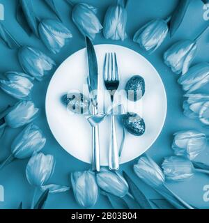 Beautiful luxury easter table cutlery settings as knife, fork with tulips, painted eggs with glitters toned in cyanotype trendy blue. Holiday background, greeting card, close up Stock Photo
