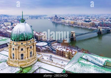 Budapest, Hungary - Aerial view of the dome of snowy Buda Castle Royal Palace from above with the Szechenyi Chain Bridge and Parliament of Hungary at Stock Photo