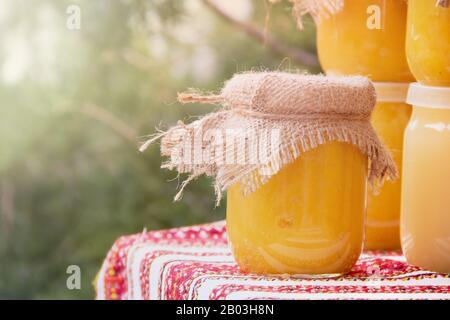 On a wooden table are glass transparent jars with different kinds of honey. Backlight, evening Stock Photo