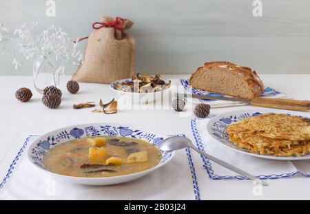 Simple substantial lunch for the cold winter season. Thick potato soup with dry mushrooms and root vegetables, with potato pancakes or rosti and glass Stock Photo