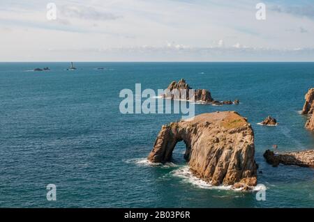 Views over the Celtic Sea from Land's End, Cornwall, with Enys Dodnan Arch in the foreground and Longships Lighthouse in the distance. Stock Photo