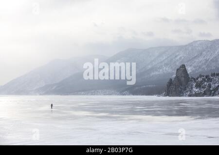 Woman walking on the frozen ice of lake Baikal on a windy day with a snow storm. Lake Baikal, Siberia, Russia. Stock Photo