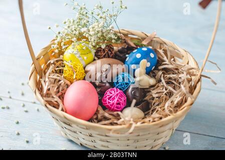 Easter gift basket with chocolate in the shape of eggs and rabbits and bright colored eggs with a spring bouquet of flowers. Stock Photo