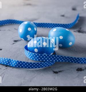Bright blue polka dot eggs with a ribbon on a gray background. Festive Easter card. Stock Photo