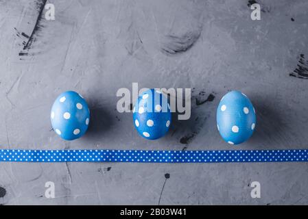 Three bright blue polka dot eggs with a ribbon on a gray background. Festive Easter card. Stock Photo
