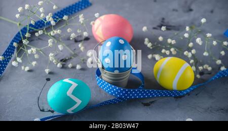 Bright colorful Easter eggs with a ribbon and spring flowers on a gray background. Festive spring Easter card. Stock Photo