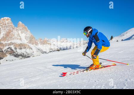 Male skier in blue and yellow clothes on slope with mountains in the background at Cortina d'Ampezzo Faloria skiing resort area Dolomiti Italy Stock Photo