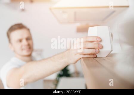 Man hand takes from shelf white ceramic mug for making breakfast coffee. Light sun, bright background Stock Photo