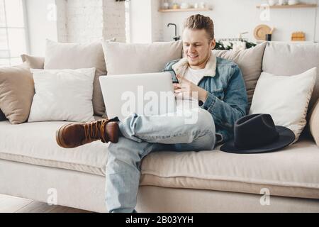 Young happy man freelancer smile works laptop computer and write message on phoneon sofa. Traveler concept Stock Photo