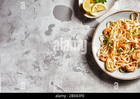 Plate of Italian noodles with scampi and a side dish of fresh lemon slices on rustic table with white distressed paint and copy space in a top down fl Stock Photo