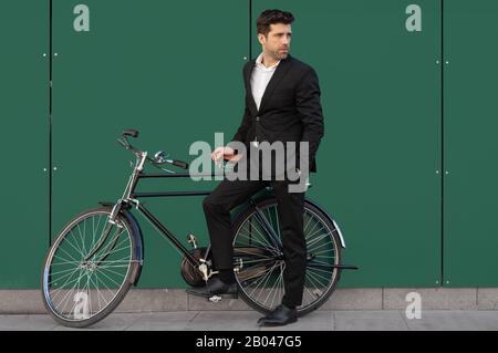 Young man in suit leaning on his classic bicycle Stock Photo