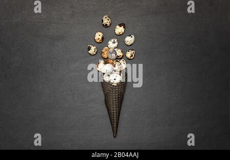 Dark waffle cone with easter eggs on a black background. Space for text. View from above. Flat lay. Stock Photo