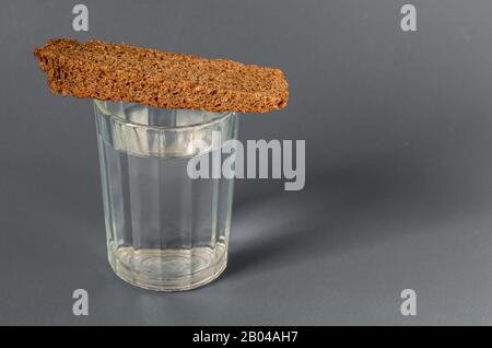 Full faceted glass of strong alcohol and bread on a gray background. Slavic traditions. Close-up. Selective focus. Stock Photo