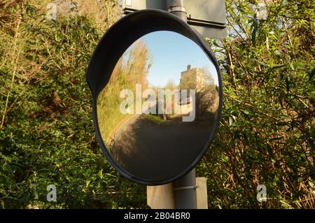 Convex mirror on signpost for observing oncoming traffic at a sharp corner. It shows the road ahead is clear. Stock Photo