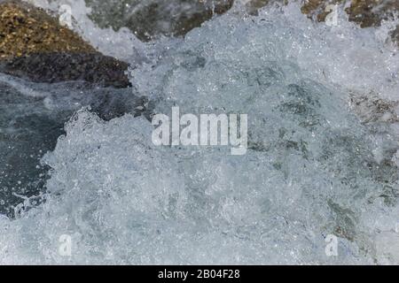 A close-up of a wave splashing over the mountain river cascade boulders: full frame stop motion shot Stock Photo