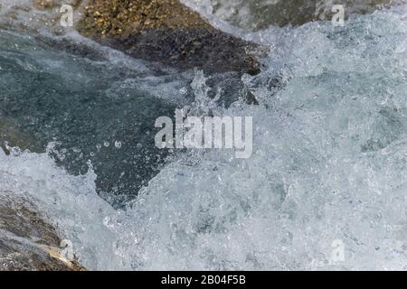 A close-up of a wave splashing over the mountain river cascade boulders: full frame stop motion shot Stock Photo