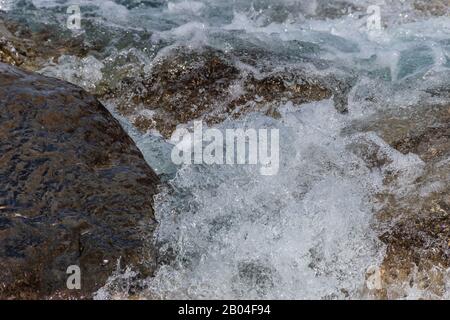 A close-up of a wave splashing over the mountain river cascade boulders: full frame stop motion shot Stock Photo