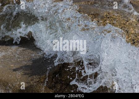 A close-up of a wave splashing over the mountain river cascade boulders: full frame stop motion shot Stock Photo
