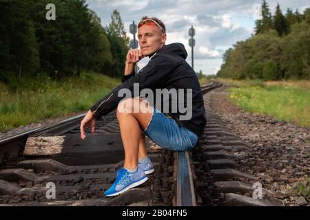 The man is sitting on the rails and thinking. Stock Photo