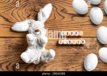 stuffed bunny with message "Hapy Easter" and many eggs on wooden background Stock Photo
