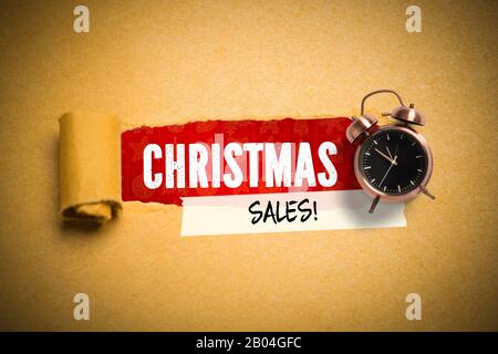 Torn paper revealing the word 'christmas sales!' besides an alarm clock Stock Photo