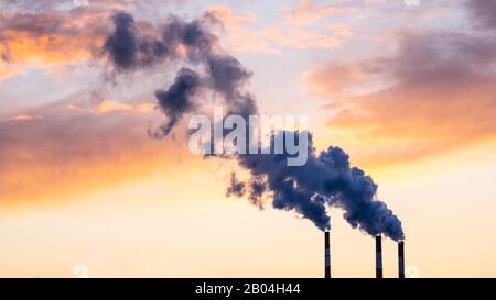 Cogeneration plant on the outskirts of a big city.  Smoke from the chimneys at sunset. Metaphor of human impact on the environment, carbon emissions. Stock Photo