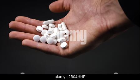 Holding medical pills and tablets and dropping them on black background Stock Photo