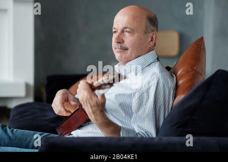 Senior man playing acoustic guitar at home enjoying the moment. Stock Photo