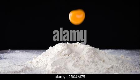 Egg falls on white flour. Ingredients for making fresh bread or pasta Stock Photo