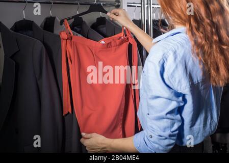 portrait of a beautiful red-haired girl, in a women's clothing store, selects and tries on a skirt from the counter. Sale of women's leather skirts, k Stock Photo