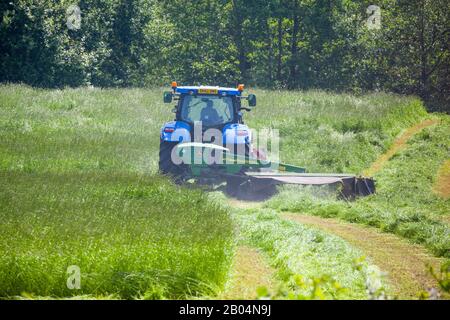 Farmer driving tractor cutting grass for silage in Cheshire farmland England UK Stock Photo