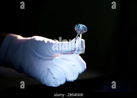 hand in white glove holding precious metal ring with big blue gem, on black background Stock Photo