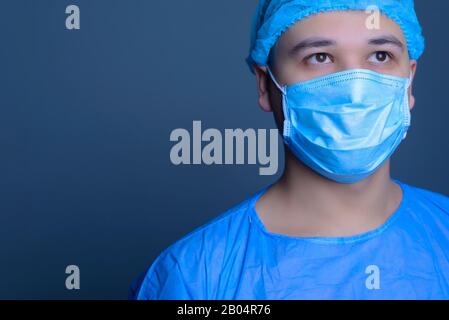 close-up portrait of a caucasian doctor surgeon, in a sterile suit, mask, looks away. On a blue background. Operating room. Surgery. Portrait of a doc Stock Photo
