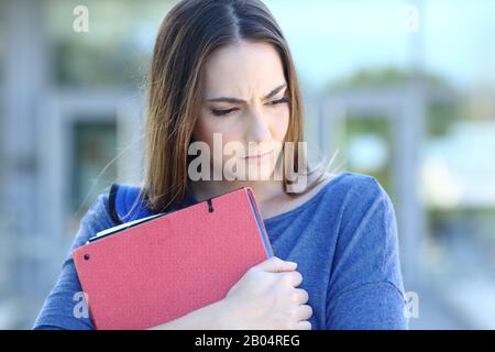 Front view portrait of a sad student looking down embracing folders walking in a college Stock Photo