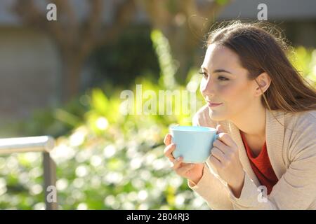 Relaxed woman holding a coffee cup contemplating sitting at the park Stock Photo