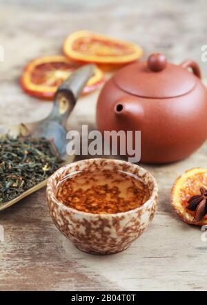 Cup of herbal tea, earthenware teapot and candied orange on the wooden table. Selective focus. Stock Photo