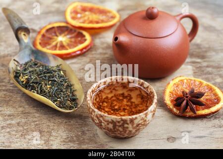 Cup of herbal tea, earthenware teapot and candied orange on the wooden table. Selective focus. Stock Photo