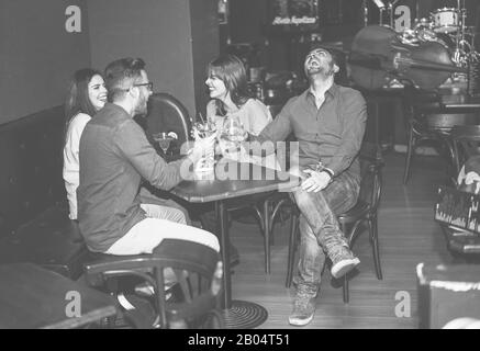 Happy friends cheering at cocktail jazz bar - Young trendy people having fun drinking alcohol and laughing - Party concept - Focus on right man hand w Stock Photo